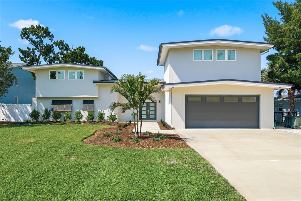 An aerial view shows a modern white house with a dark metal roof near water — 915 BAYSHORE DRIVE, TARPON SPRINGS, FL