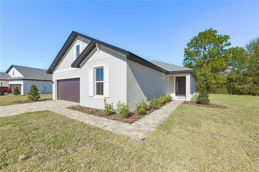A single-story house with a gray stucco exterior, a dark garage door, and a paved walkway — 17851 SW 68TH PLACE, DUNNELLON, FL