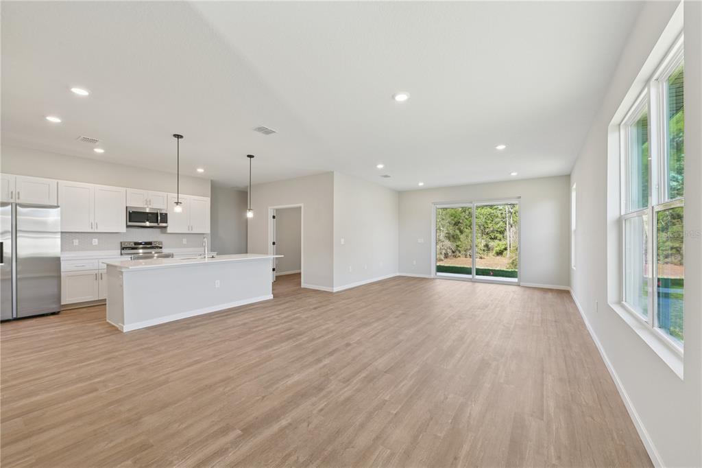 An open-concept kitchen and living area featuring white cabinets, stainless steel appliances, and wood flooring — 17851 SW 68TH PLACE, DUNNELLON, FL