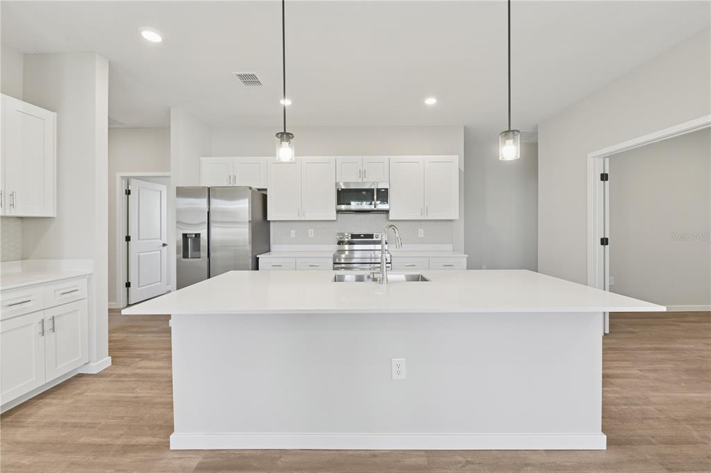 A modern kitchen features a large white island, stainless steel appliances, and white cabinetry — 17851 SW 68TH PLACE, DUNNELLON, FL