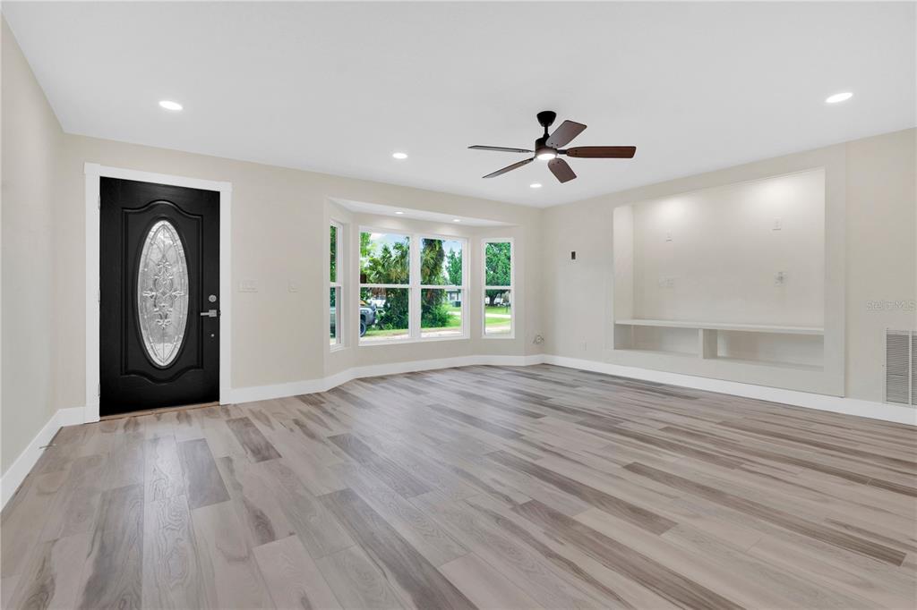 A living room with light wood-look flooring, a black front door, and a built-in wall niche — 2304 TRAVELERS PALM DRIVE, EDGEWATER, FL