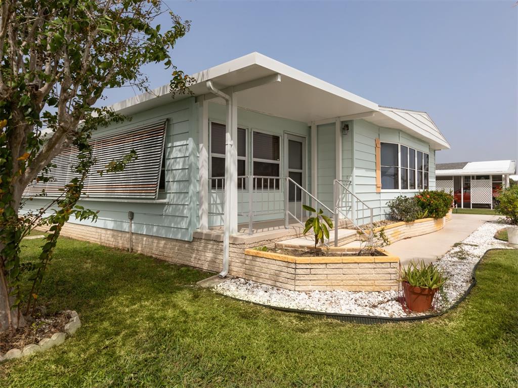A light blue mobile home with a covered porch, brick skirting, and a landscaped yard — 628 LA JOLLA CIRCLE, NORTH PORT, FL