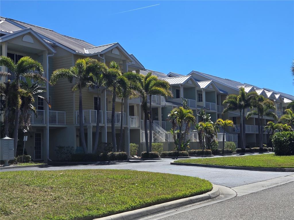 A multi-story apartment complex features yellow siding, metal roofs, and palm trees in front — 547 BAHIA BEACH BOULEVARD, RUSKIN, FL