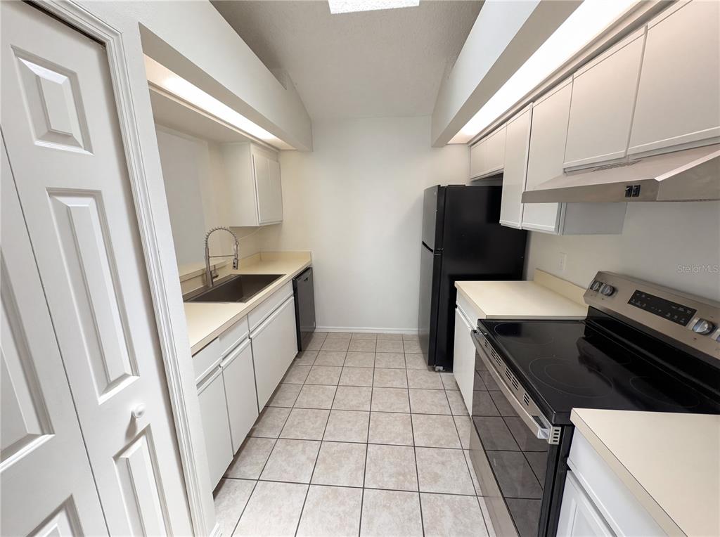 A galley-style kitchen features white cabinets, light countertops, tile flooring, and black appliances — 2000 PLAINFIELD DRIVE, ORLANDO, FL