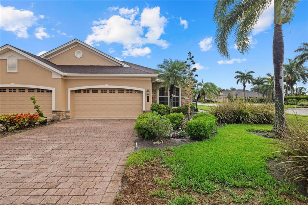 A tan house with a brick driveway, two-car garage, and palm trees under a blue sky — 4331 TURNBERRY CIRCLE, NORTH PORT, FL