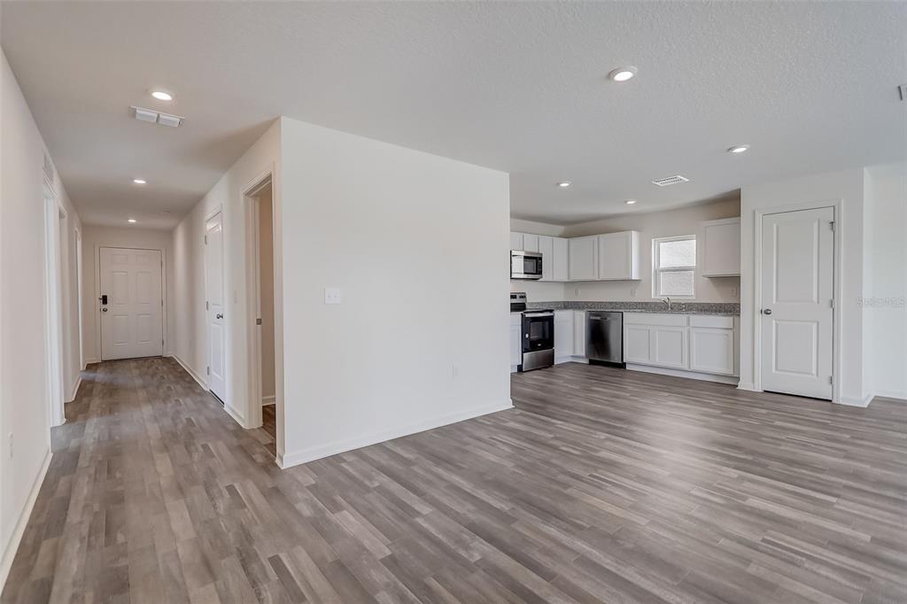 An open-concept kitchen and living area features white cabinets, stainless steel appliances, and wood-look flooring — 1455 HAYWORTH CIRCLE NW, PALM BAY, FL