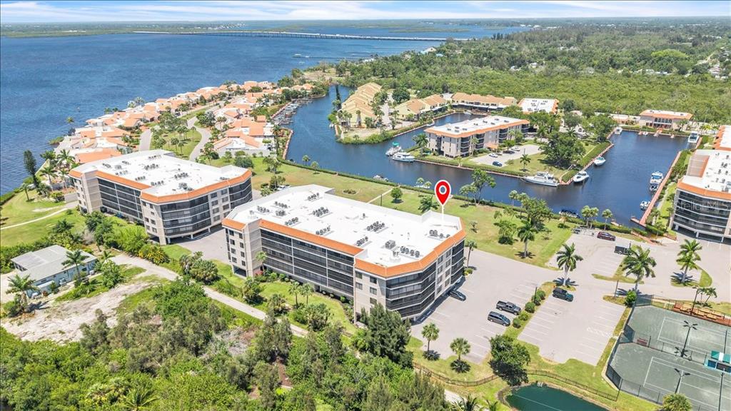 An aerial view shows multi-story waterfront residential buildings, a parking lot, and a tennis court — 25188 MARION AVENUE UNIT E101, PUNTA GORDA, FL