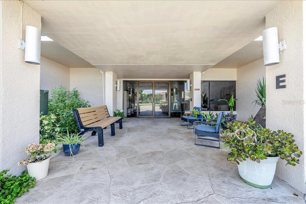 A covered outdoor entrance area features a stone patio, a bench, chairs, and potted plants — 25188 MARION AVENUE UNIT E101, PUNTA GORDA, FL