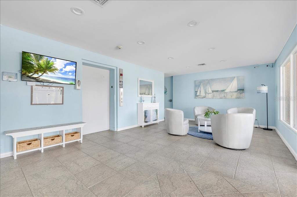 A light blue lobby features tile floors, white armchairs, and a wall-mounted television — 25188 MARION AVENUE UNIT E101, PUNTA GORDA, FL