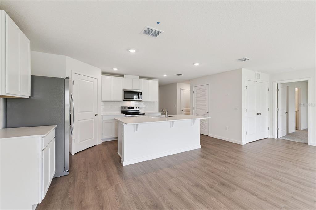 A modern kitchen features white cabinetry, a central island, stainless steel appliances, and wood-look flooring — 1314 CONGO DRIVE, POINCIANA, FL