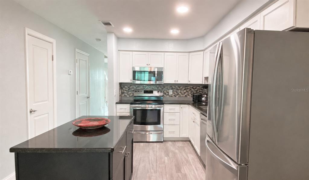 A kitchen features white cabinets, stainless steel appliances, a dark island, and a mosaic backsplash — 5500 OCEAN SHORE BOULEVARD UNIT UT23, ORMOND BEACH, FL