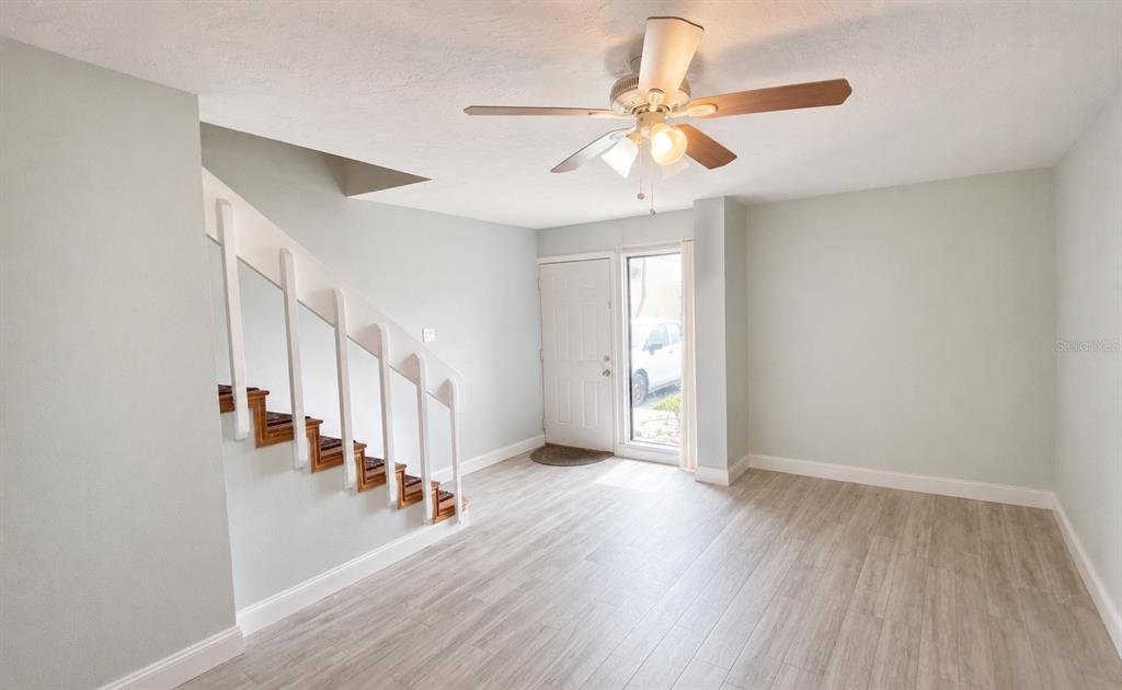 An entryway with light wood-look flooring, a white staircase, and a ceiling fan — 5500 OCEAN SHORE BOULEVARD UNIT UT23, ORMOND BEACH, FL