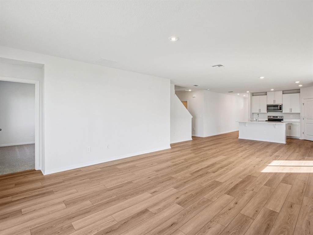 An open-concept living area features light wood-look flooring, white walls, and a modern kitchen — 7176 RAY CREEK DRIVE, BROOKSVILLE, FL