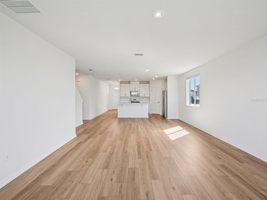 An open-concept living area features light wood-look flooring, white walls, and a kitchen island — 7176 RAY CREEK DRIVE, BROOKSVILLE, FL