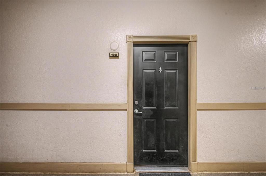 A black front door with a number plate is set in a beige wall — 501 KNIGHTS RUN AVENUE UNIT 2211, TAMPA, FL