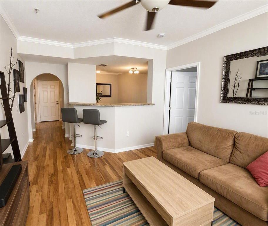 A living room with wood flooring, a brown sofa, and a breakfast bar with two stools — 501 KNIGHTS RUN AVENUE UNIT 2211, TAMPA, FL