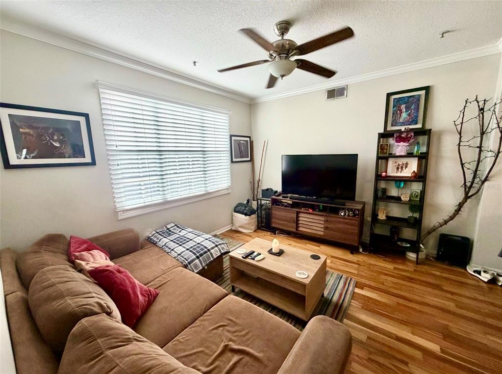 A living room features a brown sectional sofa, a television on a wooden stand, and shelving — 501 KNIGHTS RUN AVENUE UNIT 2211, TAMPA, FL