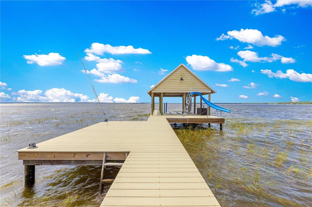 A wooden dock leads to a covered boat slip with a blue slide on a lake — 12360 E HIGHWAY 25, OCKLAWAHA, FL