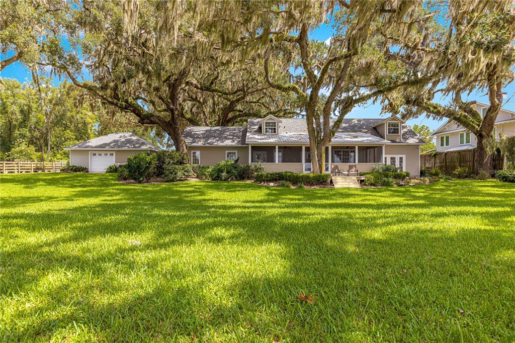 A tan house with a screened porch and a detached garage sits on a grassy lawn — 12360 E HIGHWAY 25, OCKLAWAHA, FL