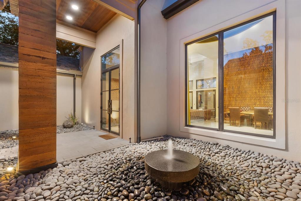 A modern courtyard features a stone fountain, pebble ground cover, and a large glass window — 49 OSPREY POINT DRIVE, OSPREY, FL