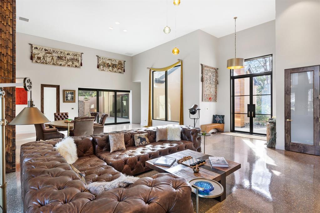 A spacious living room features a large tufted leather sectional, high ceilings, and polished floors — 49 OSPREY POINT DRIVE, OSPREY, FL