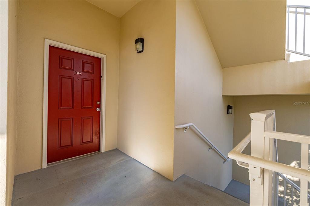 A red apartment door with unit number 2-203 sits at the top of a concrete staircase — 921 BEGONIA ROAD UNIT 203, CELEBRATION, FL