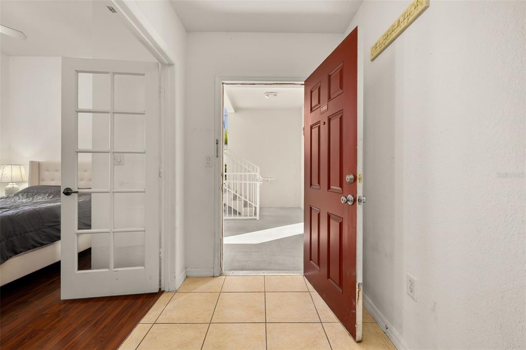 An open red front door reveals an exterior staircase, adjacent to a bedroom with French doors — 921 BEGONIA ROAD UNIT 203, CELEBRATION, FL