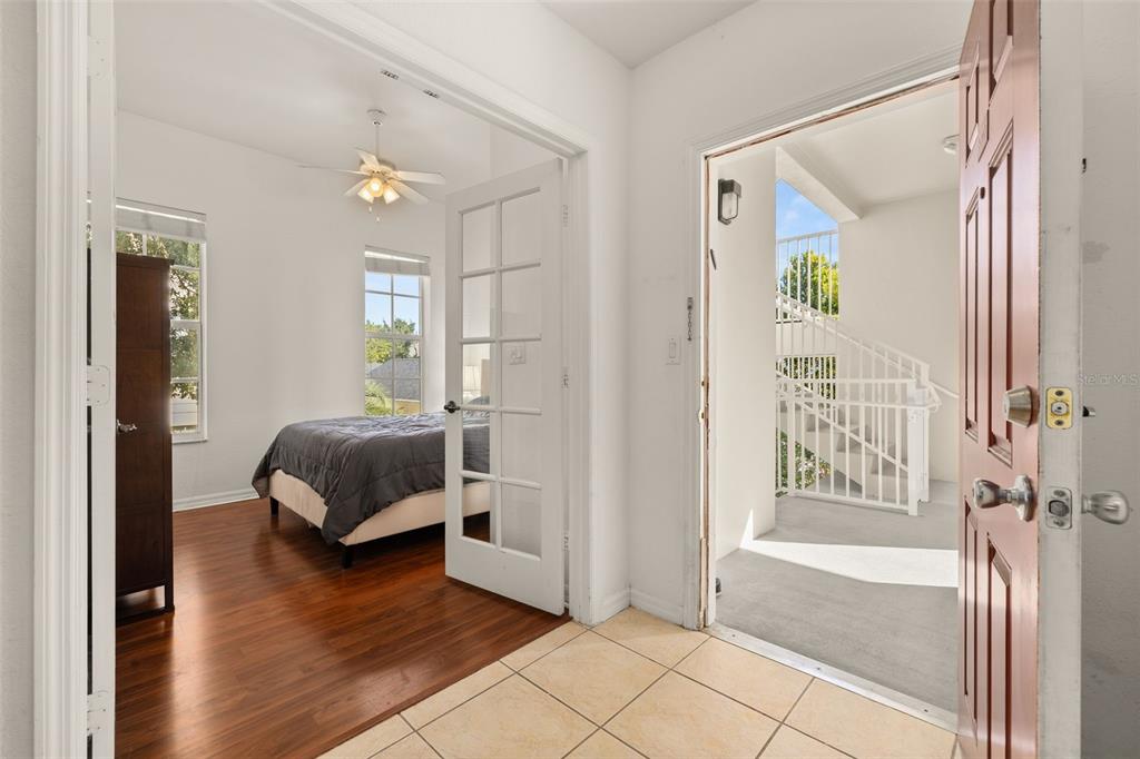An entryway with tile flooring leads to a bedroom with wood floors and an exterior staircase — 921 BEGONIA ROAD UNIT 203, CELEBRATION, FL