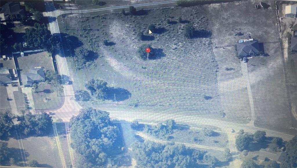 An aerial view shows a vacant, grassy lot with a few trees and a red marker — 000 SE SUNSET HARBOR ROAD, SUMMERFIELD, FL