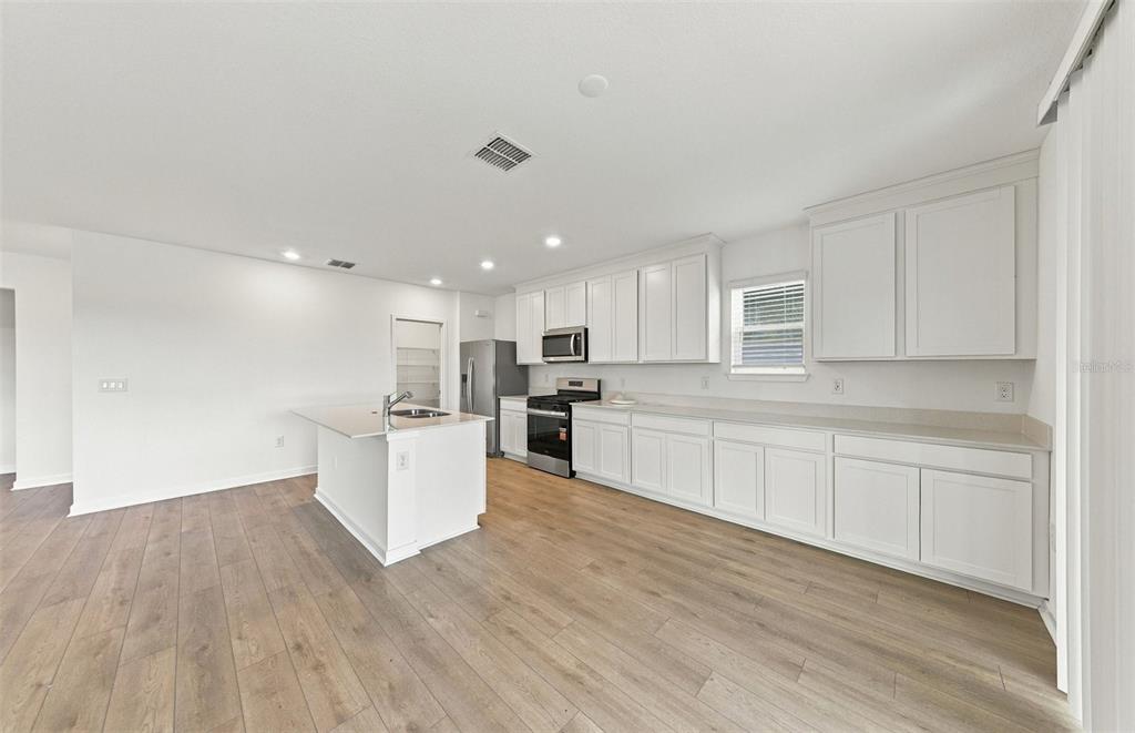 A bright kitchen features a white island, stainless steel appliances, and an adjacent dining area — 9185 NEWMONS PLACE, WILDWOOD, FL