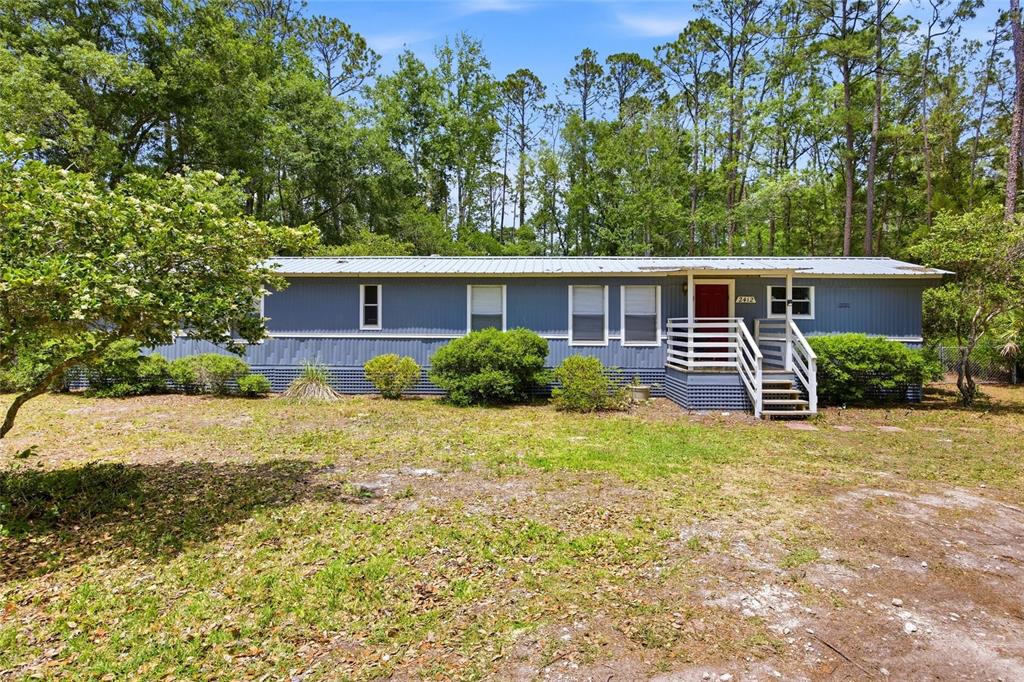 The exterior of a manufactured home features a red front door and a wooden porch — 2412 NW 116TH PLACE, GAINESVILLE, FL