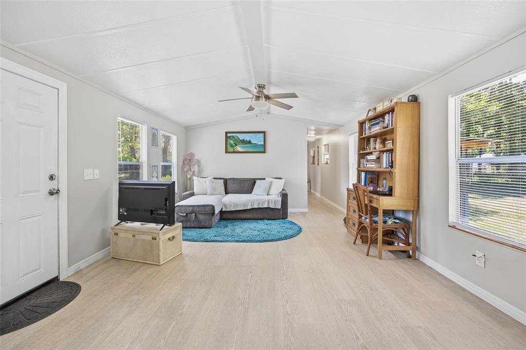 A living room features light wood flooring, a grey sectional sofa, and a wooden bookshelf desk — 2412 NW 116TH PLACE, GAINESVILLE, FL