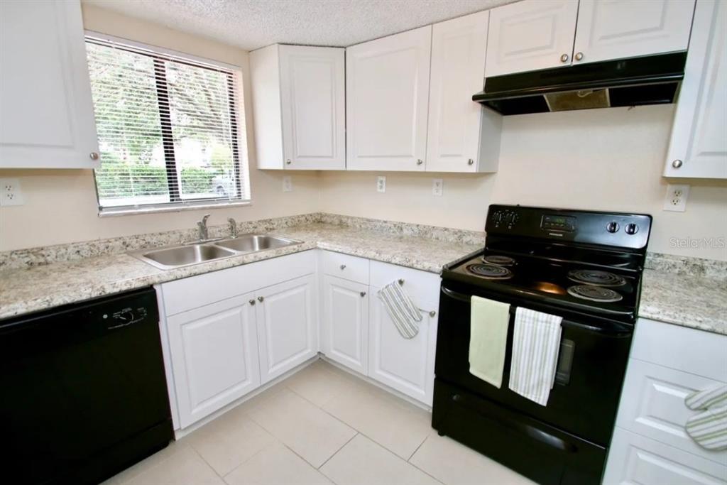 A kitchen features white cabinets, black appliances, and speckled countertops — 1350 VIRGINIA AVENUE UNIT 19, DAYTONA BEACH, FL