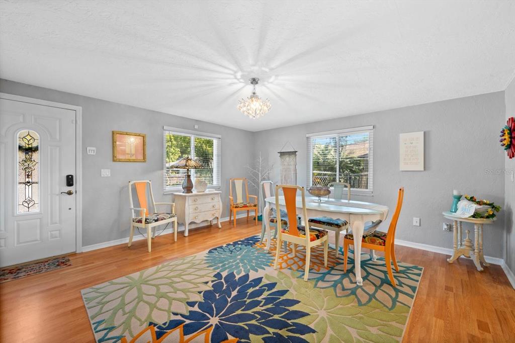 A dining room with a floral area rug, orange-accented chairs, and a crystal chandelier — 5027 31ST STREET W, BRADENTON, FL