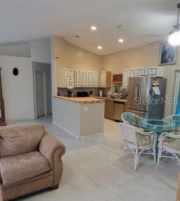 A kitchen with white cabinets, stainless steel appliances, and a breakfast bar near a dining area — 5411 THOMAS STREET, BOKEELIA, FL
