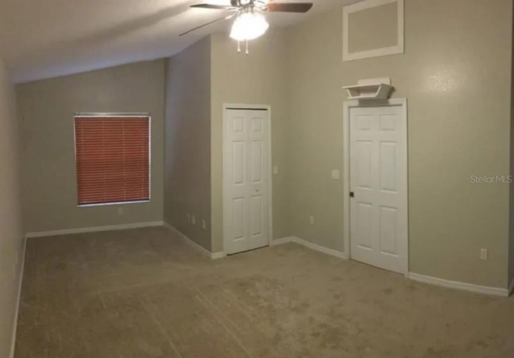 An empty bedroom features beige carpet, a vaulted ceiling with a fan, and two white doors — 5411 THOMAS STREET, BOKEELIA, FL