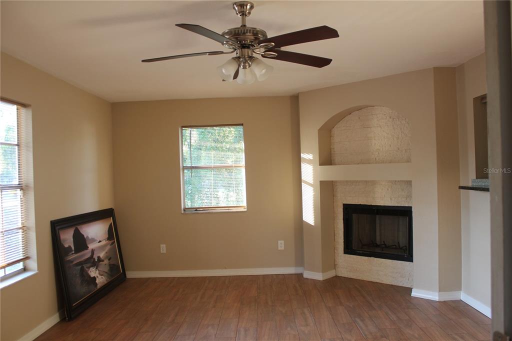 A living room features wood-look tile flooring, a ceiling fan, and a corner fireplace — 9082 ACORN BOULEVARD, PUNTA GORDA, FL
