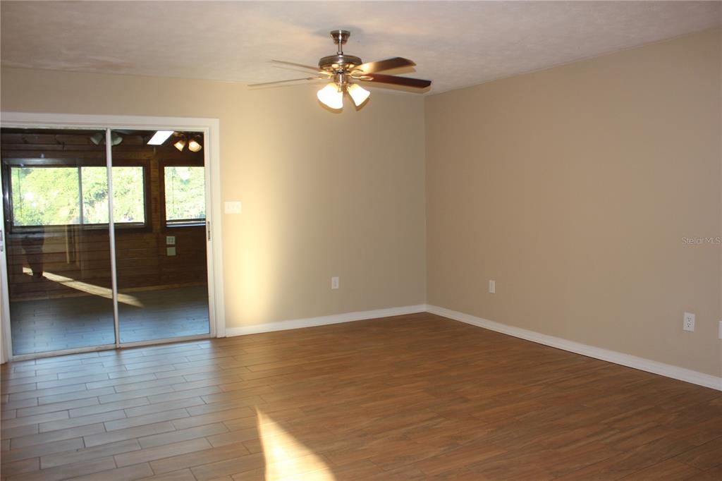 A living room with wood-look tile flooring, beige walls, a ceiling fan, and sliding doors — 9082 ACORN BOULEVARD, PUNTA GORDA, FL
