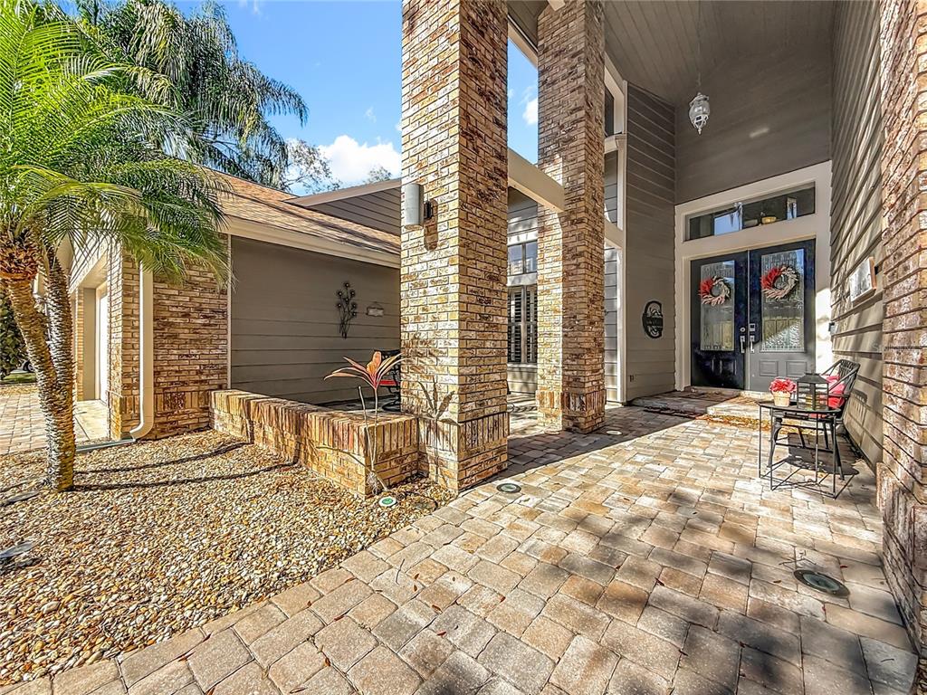 A brick-columned entryway leads to a dark double door with a paved patio area — 50 WILLOWOOD LANE, OLDSMAR, FL