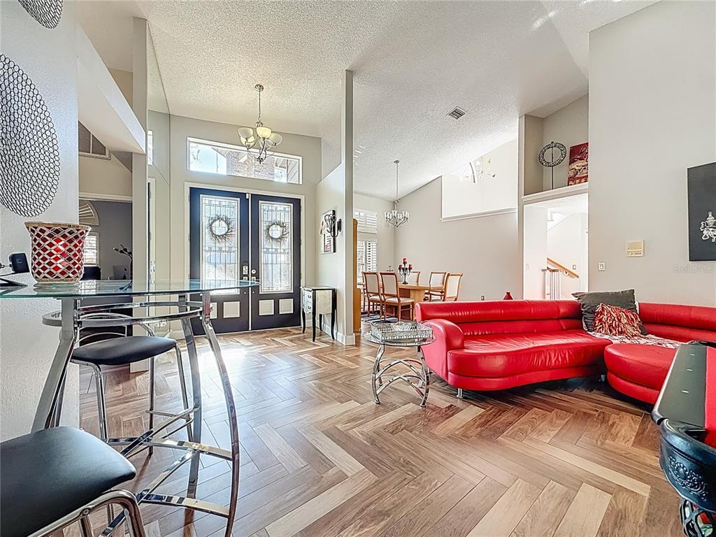 A bright living room features herringbone wood floors, a red sofa, and a glass table — 50 WILLOWOOD LANE, OLDSMAR, FL