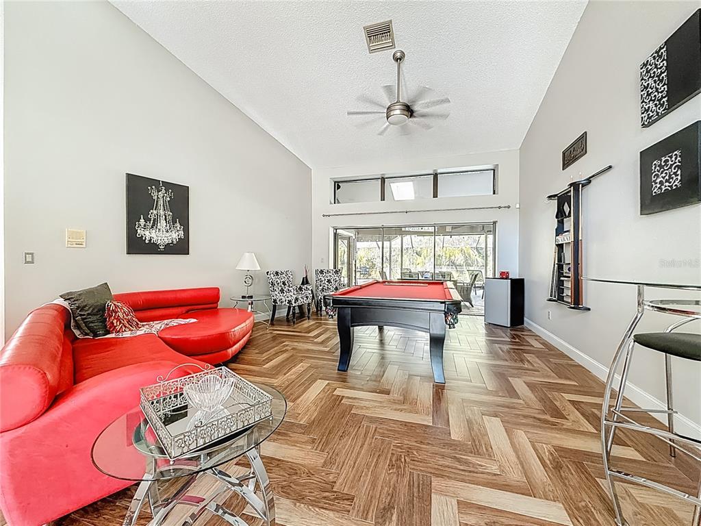 A living room features a red sectional sofa, a pool table, and herringbone-patterned wood flooring — 50 WILLOWOOD LANE, OLDSMAR, FL
