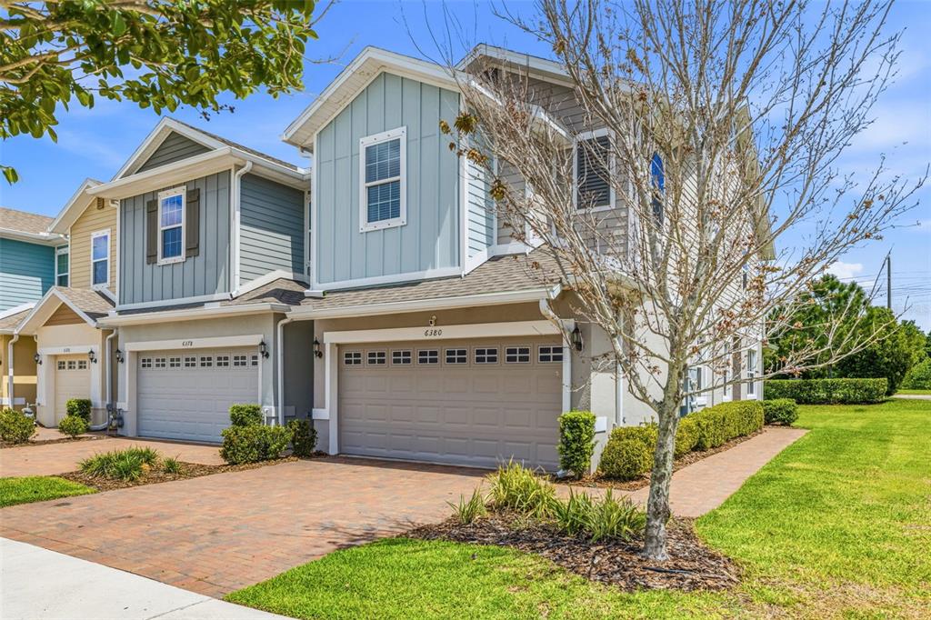A two-story suburban townhouse with a light blue facade, tan garage, and brick paver driveway — 6380 CAMINO DRIVE, APOLLO BEACH, FL