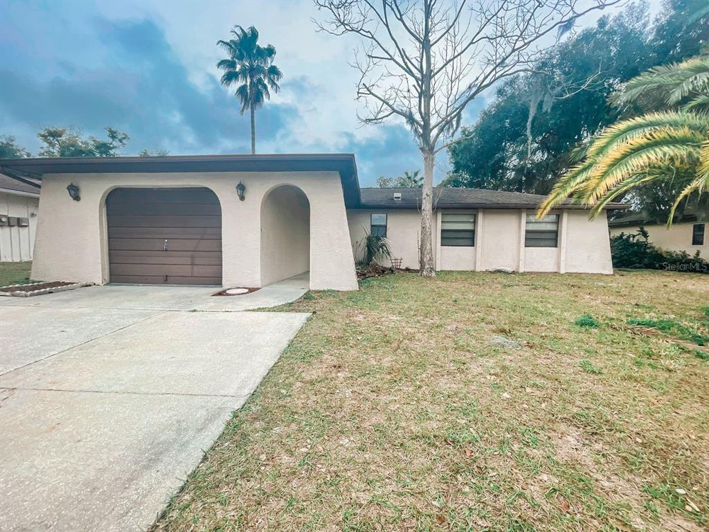 A single-story house with a beige stucco exterior, a one-car garage, and a front lawn — 12834 LAKE TREE LANE, HUDSON, FL