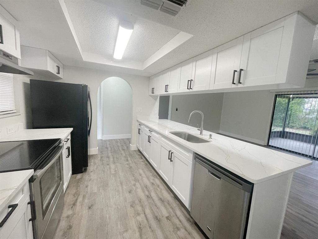 A kitchen with white cabinets, quartz countertops, stainless steel appliances, and wood-look flooring — 12834 LAKE TREE LANE, HUDSON, FL
