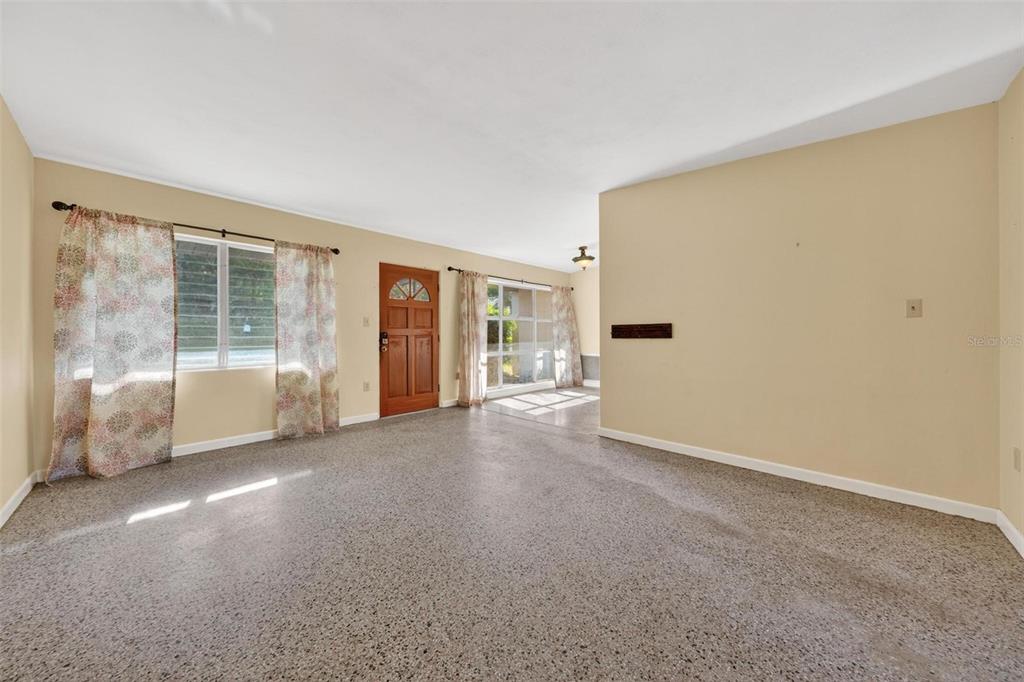 A living room features speckled flooring, beige walls, a wooden front door, and floral curtains — 710 TWIN OAKS LANE, EUSTIS, FL