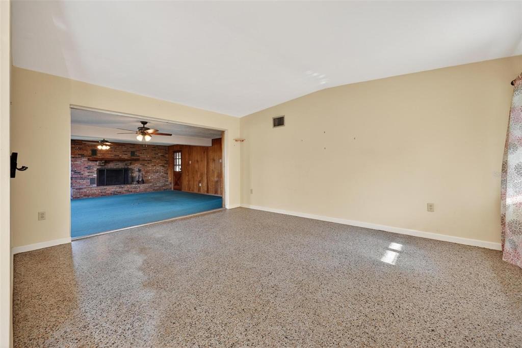 A living room with terrazzo flooring opens into a sunken den featuring a brick fireplace — 710 TWIN OAKS LANE, EUSTIS, FL
