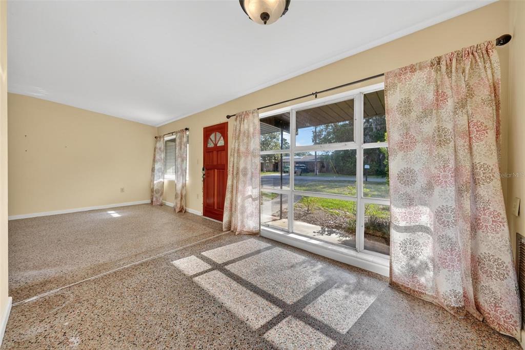 A room with terrazzo flooring, a large window, a red front door, and patterned curtains — 710 TWIN OAKS LANE, EUSTIS, FL