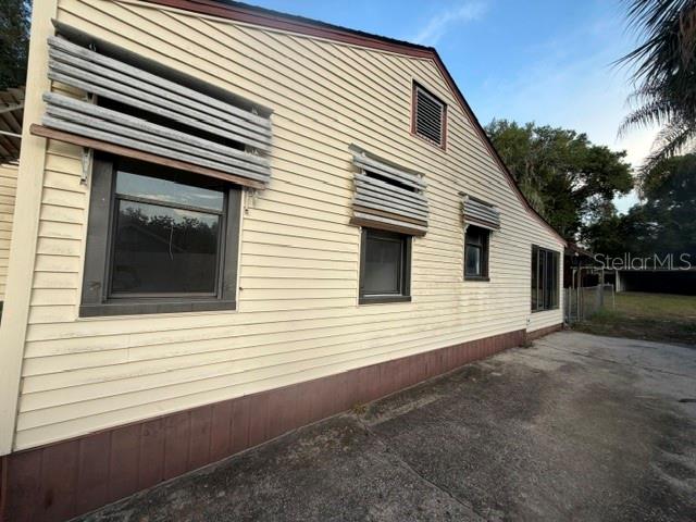 The exterior side of a house features light-colored siding, metal window awnings, and concrete ground — 1607 CENTER STREET, LEESBURG, FL
