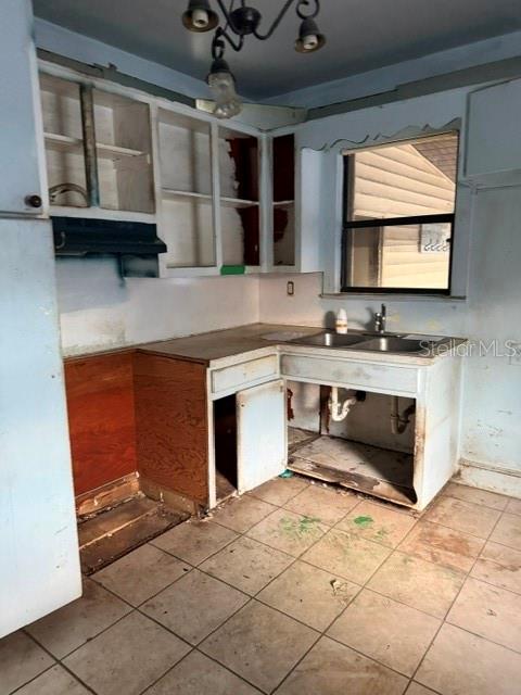A dilapidated kitchen features unfinished wooden cabinets, an exposed sink plumbing area, and tiled flooring — 1607 CENTER STREET, LEESBURG, FL
