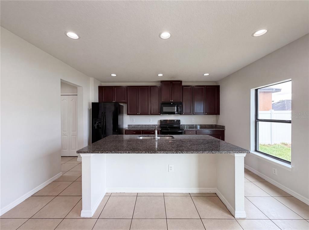 A kitchen features dark wood cabinets, granite countertops, a central island, and tile flooring — 14207 ALISTAR MANOR DRIVE, WIMAUMA, FL